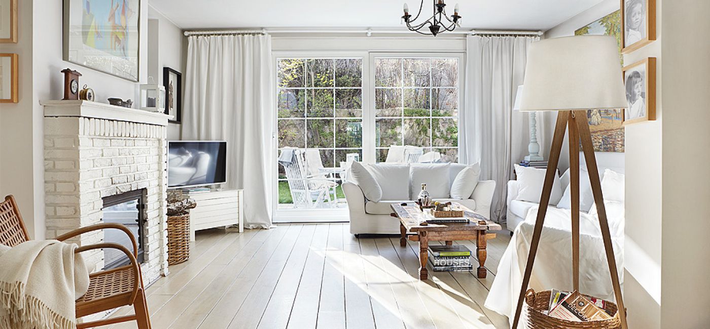 Salon w bieli. Zamiast marmuru wokół kominka cegła i drewniane decha pomalowana na biało.