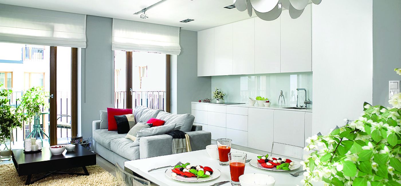 Szafki kuchenne zrobione na zamówienie z lakierowanego MDF-u. Sofa marki Dublo, dywan, szare poduchy i koc - Belbazaar.