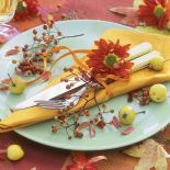 Jesienny miszmasz na stole: kwiaty, gałązki jarzębiny, małe jabłuszka i kolorowe liście