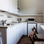 Białe szafki zamontowano tylko na jednej ścianie. Na drugiej powieszono półkę.