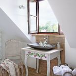 Biały stolik i krótki rzucik filoletowych jeżyn - idealny mebel-dekoracja do łazienki w stylu prowansalskim.