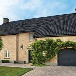 Ceglana elewacja, czarny spadzisty dach i minimalistyczny ogród.