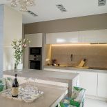 Chłodny kamień i fronty na wysoki połysk ocieplaja krzesła obite lnem marki Christopher Farr.