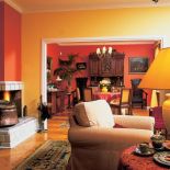 Ciepłe kolory dodają wnętrzu przytulności. W salonie trzy ściany są żółte, a jedna pomarańczowa - w tym samym kolorze,