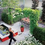 Czerwone akcenty w ogrodzie nawiązują do mebli w kuchni. Zielone kule w wysokich donicach to strzyżony bukszpan. W sadzwce