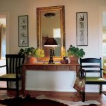 Drewniana konsola, krzesła, lustro, ramki ze zdjęciami tworzą w holu symetryczną kompozycje.