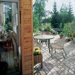 Drewniany taras otacza ogród pełen drzew i kwiatów.