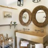 Kamienna podłoga i umywalka komponują się z drewnianymi ramami luster i lampionami.