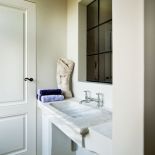 Kamienna umywalka obok chromowanej baterii, zabawne okucia, tkaniny i trochę sztuki.