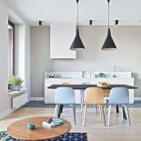 Kuchnia urządzona na biało, ale ciepły ton nadają jej nowoczesne krzesła w kolorze naturalnego drewna i gołębiego błękitu.