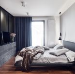 Lekko mroczna sypialnia z dużym łóżkiem. Dominują w niej szarości i miękkie materiały. Kontrastem jest