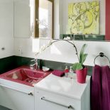 Meble i płytki są biale. Jedyne ekstrawagancje to purpurowa umywalka i kolejny obraz z seriii żółte pomidory.