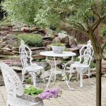 Miejsce do wypoczynku obok sadzawki z wodospadem. Metalowy stolik i krzesła w stylu rustykalnym podkreślają