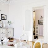 Na biało pomalowano stół, krzesła w stylu Ludwika i rzeźbioną komodę.