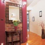 Na ceglanej ścianie wisi lustro w drewnianej ramie.