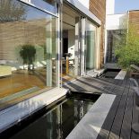 Na drewnianym tarasie jest mostek. Pod nim w betonowym korycie wyłożonym otoczakami płynie woda.