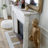 Na marmurowym portalu kominka stoi lustro w złoconej ramie i dalekowschodnie figurki.