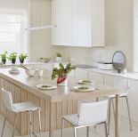 Na podłodze leży wapień perlino bianco. Matowe szafki zestawiono z wyspą-stołem z szarzonego dębu. Sprzęt