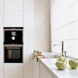 Na podłodze leży wapień perlino bianco. Matowe szafki zestawiono z wyspą-stołem z szarzonego dębu. Sprzęt