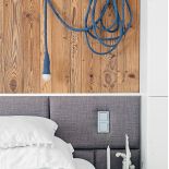 Na ścianie szarej sypialni w stylu skandynawskim jest wiekowe drewno.