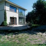 Na tarasie stoją meble ogrodowe. Nad rzeczką, pośród traw