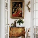 Nad komodą wisi obraz w zloconej ramie.