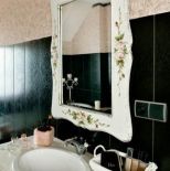 Nad umywalką wisi lustro w zdobionej ramie.