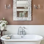 Nad wanną wiszą eleganckie kinkiety i lustro w bogato zdobionej ramie.