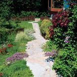 Nierówna, wyłożona kamieniem alejka, drewniane płotki i kępki roślin rozsiane, jakby same tak wyrosły - ot, wiejski ogródek.