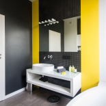 Nowoczesną i monochromatyczną aranżację łazienki dynamizują żółte pasy między płytkami.