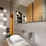 W ŁAZIENCE DZIECI POŁĄCZONO SZARE PŁYTKI O HEKSAGONALNYCH KSZTAŁTACH Z PROSTYMI PANELAMI Z NATURALNEGO DREWNA.