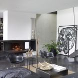 Otwarty kominek w czarnej ramie. Można sie przy nim ogrzać, siedzac na klasyku: bujanym krześle Eamesów.