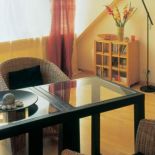 Plecione fotele, stół ze szklanym blatem i niska biblioteczka,