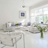 Salon z wielkimi oknami i piecem kaflowym. Fioletowe akcenty przełamują biel.