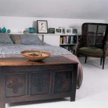 Przy łóżku stoi skrzynia zdobiona ornamentami roślinnymi.