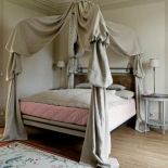 Przy łóżku z baldachimem stoją stoliki i lampki.