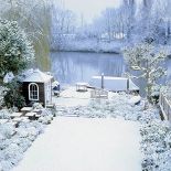 Rzeka, zmrożona, odbija światła domów, które przycupnęły na brzegu.