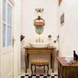 Ściany bielone gruboziarnistym tynkiem, bateria z targu staroci, wiekowa rama lustra, stuletnia kratka do osłonięcia