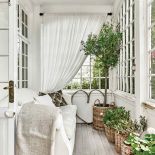 WERANDA OD FRONTU DOMU TO IDEALNE MIEJSCE DO ODPOCZYNKU. STOJĄ TU JASNA KANAPA I OCZYWIŚCIE ROŚLINY – DUŻE DRZEWKO