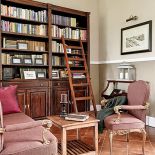 Styl starej Anglii, stonowane kolory, drewniane lamperie na ścianach, ciemna kanapa, nobliwa biblioteka z okazałym