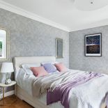 Prosto urządzona, ale przytulna sypialnia. Na ścianie tapeta z Riviera Maison, lampa z kryształową nogą