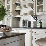 Stylizowana, biała kuchnia. Półki z dekoracyjnymi, żeliwnymi wspornikami. FABRYKA WNĘTRZ