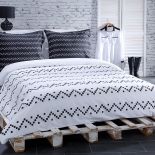 Sypialnia urządzona niskim kosztem: łóżko z palet, na ścianie tapeta imitująca cegły. Minimalizm aranżacji podkreśla