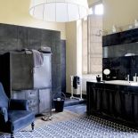 Szafę tak pomalowano, żeby zlala się w jedno z ciemnymi plytkami z polerowanego betonu. Fotel w aksamitnym obiciu, drewno