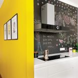 Szafki zrobione z matowego mdf-u, do tego biały blat z korianu. Dla kontrastu, czarna ściana pomalowana farbą tablicową.