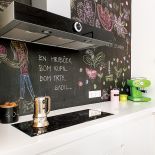 Szafki zrobione z matowego mdf-u, do tego biały blat z korianu. Dla kontrastu, czarna ściana pomalowana farbą tablicową.