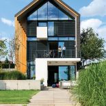 Szklana ściana domu znajduje się od strony południowej. Pod tarasami spływa ogród.