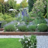 Tradycyjne rośliny, jak bukszpany i róże, połączone są z nowoczesną architekturą. Stąd stalowe elementy i chromowane donice.