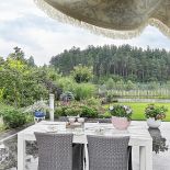 Urządzony naturalnie, sielsko: stół, plecione fotele, kwiaty.