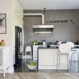 W kuchni czarna lodówka, podłoga z samopoziomującego się betonu i wyspa z polerowanego kamienia.